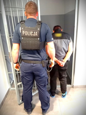 Na zdjęciu policjant stoi obok zatrzymanego, który zostaje umieszczany w policyjnej celi.