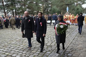 Na zdjęciu kobieta i dwóch mężczyzna idą złożyć kwiaty.