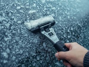 Na zdjęciu dłoń ze skrobaczką podczas skrobania zamarzniętej szyby.