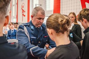 Na zdjęciu Komendant Powiatowy Policji w Będzinie zakłada biało-czerwoną opaskę uczennicy.
