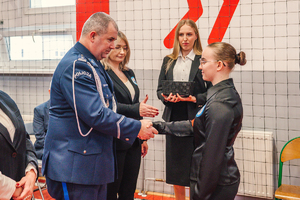 Na zdjęciu Komendant Powiatowy Policji w Będzinie gratuluje uczennicy i podaje dłoń.