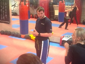 Na zdjęciu mężczyzna w koszulce z napisem policja patrzy się na kobietę na sali treningowej.