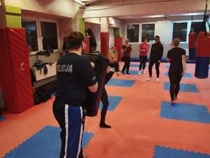 Na zdjęciu mężczyzna w koszulce policyjnej trzyma tarczę, a kobieta w nią kopie.