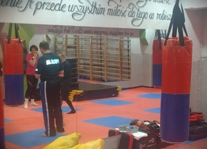 Na zdjęciu mężczyzna w koszulce policyjnej mówi do kobiet na sali treningowej.