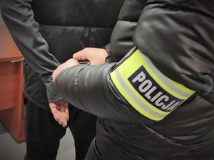 Na zdjęciu zbliżenie na policjanta kryminalnego, który ma założoną opaskę z napisem POLICJA.