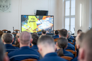 Zdjęcie grupowe przedstawiające zgromadzonych policjantów i zaproszonych gości w sali sesyjnej Starostwa Powiatowego w Będzinie, w oddali widać film puszczany na telewizorze.