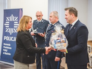 Komendant Powiatowy Policji w Będzinie oraz Starosta Będziński wyróżniają pracowników z okazji Święta Służby Cywilnej, starosta wręcza upominek.