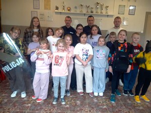Zdjęcie grupowe dwóch policjantów z grupą młodzieży podczas spotkania dotyczącego bezpiecznych ferii.