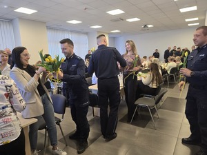 Zdjęcie grupowe. Policjanci w mundurach wręczają kobietom kwiatki.