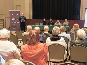 Zdjęcie grupowe podczas debaty na temat bezpieczeństwa seniorów na sali konferencyjnej. Widzimy seniorów, policjantów i zaproszonych prelegentów.
