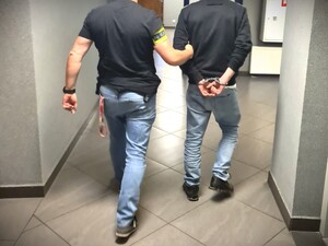 Na zdjęciu zatrzymany mężczyzna prowadzony przez policjanta kryminalnego.