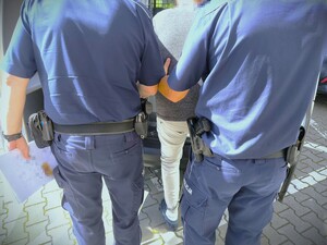 Na zdjęciu widzimy jak dwóch policjantów doprowadza zatrzymanego do radiowozu.