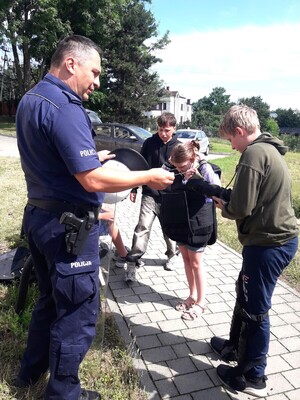 Na zdjęciu policjant pomaga młodzieży założyć elementy policyjnego wyposażenia.