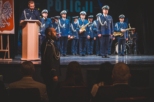 Zdjęcie grupowe w teatrze przedstawiające policjantów. Policjant na przodzie stoi na baczność.