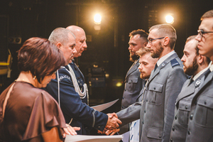 Zdjęcie grupowe w teatrze przedstawiające policjantów występujących do mianowania na scenie z Zastępcą Komendanta Wojewódzkiego Policji w Katowicach oraz Komendantem Powiatowym Policji w Będzinie, którzy składają policjantom gratulacje.