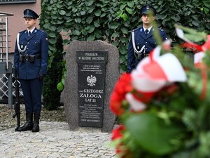 Zdjęcie przedstawia biało-czerwone kwiaty oraz policjantów z warty honorowej, którzy stoją przy pomniku poległego będzińskiego policjanta.